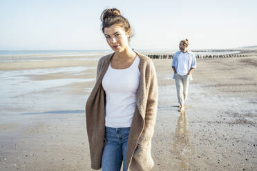 Young woman walking on beach with boyfriend in background at beach - UUF22727