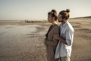 Young man embracing girlfriend while standing on beach during sunny day - UUF22733