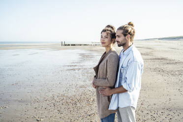 Young couple day dreaming together while standing on beach - UUF22735