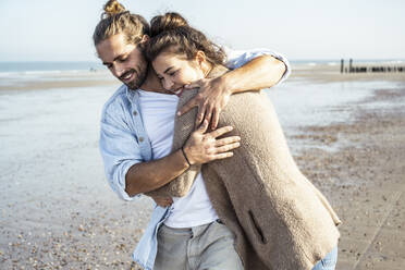 Smiling girlfriend embracing boyfriend at beach on sunny day - UUF22742