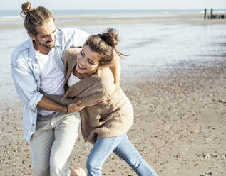 Cheerful young couple walking while embracing at beach during weekend - UUF22743