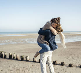 Young man picking up girlfriend and embracing at beach on sunny day - UUF22745