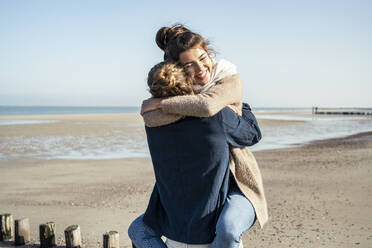 Zärtliches junges Paar umarmt sich am Strand an einem sonnigen Tag - UUF22747