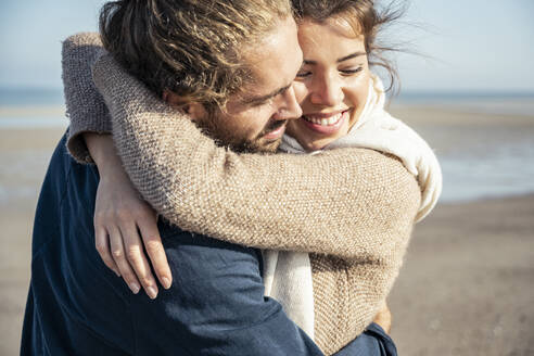 Glückliches junges Paar umarmt sich am Strand an einem sonnigen Tag - UUF22748