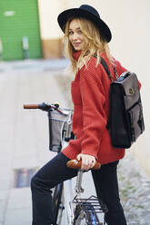 Blonde Frau, die einen Rucksack trägt, während sie mit dem Fahrrad auf dem Gehweg steht - JSMF01896