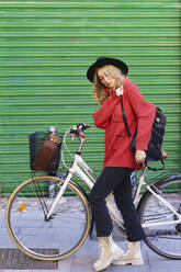 Woman wearing backpack while standing with bicycle on footpath - JSMF01903