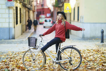 Carefree woman looking away while standing with bicycle on road - JSMF01924