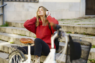 Blonde Frau hört Musik über Kopfhörer, während sie auf einer Treppe sitzt - JSMF01947
