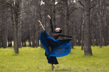 Professional ballet dancer dancing while standing in forest - JCCMF01027