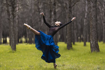 Young ballet dancer with hand raised dancing while standing in forest - JCCMF01028