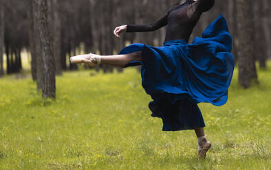 Ballet dancer wearing ballet shoe dancing while standing in forest - JCCMF01029