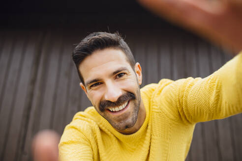 Smiling man with mustache in yellow sweater taking selfie - MIMFF00553