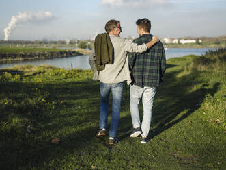 Father arm around son walking at riverbank - GUSF05171