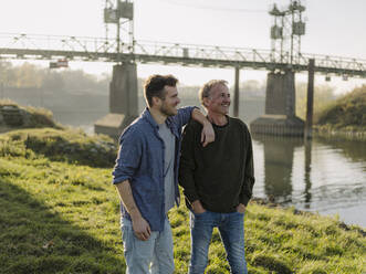 Sohn steht neben lächelndem Vater am Flussufer - GUSF05174