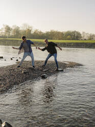 Father and son throwing pebbles in river during autumn - GUSF05175