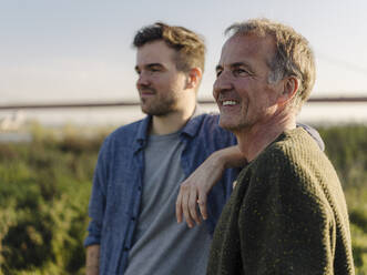 Thoughtful father and son looking at riverbank - GUSF05178