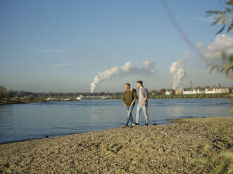 Sohn spricht mit Vater beim Spaziergang gegen den Himmel am Flussufer - GUSF05183