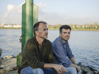 Nachdenklicher Vater und Sohn sitzen auf einem Felsen am Fluss - GUSF05195