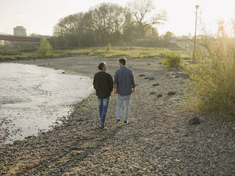 Father and son walking at riverbank during autumn - GUSF05203