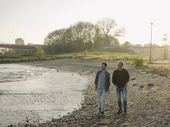 Son and father looking away while walking at riverbank - GUSF05204