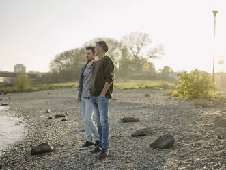 Son standing with father at riverbank during autumn - GUSF05205