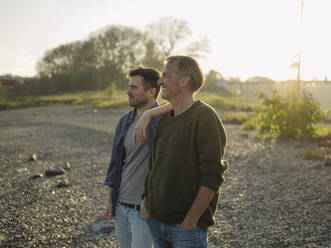 Thoughtful son and father smiling while standing at riverbank - GUSF05206