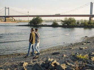 Father and son admiring river while standing against sky - GUSF05212