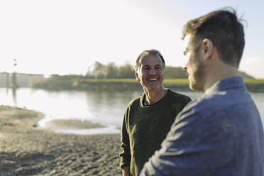 Happy father talking with son at riverbank on sunny day - GUSF05239