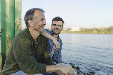 Smiling son looking at happy father against river and sky - GUSF05257