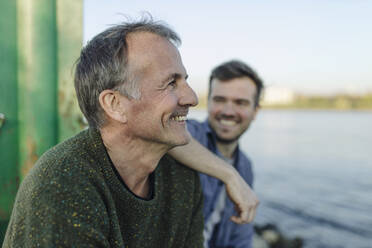 Smiling son looking at happy father against river - GUSF05258