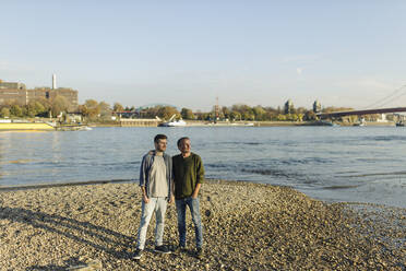 Son and father looking away while standing against river on sunny day - GUSF05264