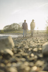 Father and son walking on riverbank at evening - GUSF05266