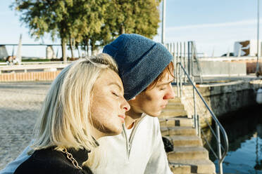 Junges Paar mit geschlossenen Augen entspannt sich am Hafen während eines sonnigen Tages - XLGF01089