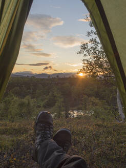 Älterer männlicher Wanderer im Zelt bei Sonnenuntergang im Wald in Schweden - HUSF00203