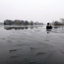Germany, Berlin, Ice floating in river Spree with boat sailing in background - ALEF00110