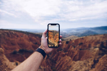 Unkenntlich gemachter männlicher Wanderer, der mit seinem Handy ein Bild der erodierten Berglandschaft schießt, während er durch das Hochland reist und die wilde Natur erkundet - ADSF20523