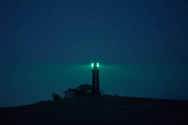 Bakenturm auf einem Hügel, der die Dunkelheit mit grünem Licht vor dem Hintergrund des nächtlichen Sternenhimmels erhellt - ADSF20531