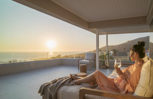 Frau genießt Weißwein und Sonnenuntergang Blick auf den Ozean auf Luxus-Balkon - CAIF30227