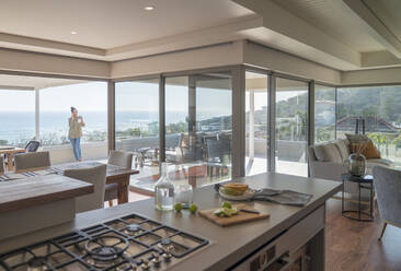 Frau mit Kaffee, die auf einem Balkon mit Meerblick mit ihrem Smartphone spricht - CAIF30239