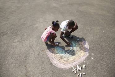 Brother and sister drawing rainbow with sidewalk chalk on pavement - CAIF30247