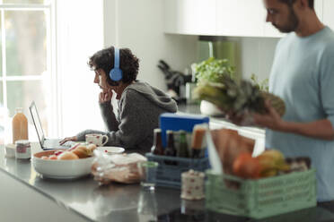 Couple working from home and unloading groceries in kitchen - CAIF30263