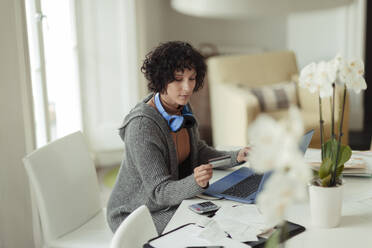 Woman with credit card paying bills at laptop at dining table - CAIF30264