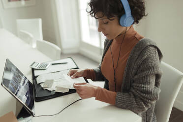 Woman with headphones and receipts paying bills at digital tablet - CAIF30270