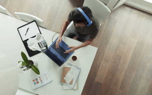 Mann mit Kopfhörern arbeitet von zu Hause aus am Laptop auf dem Esstisch - CAIF30272