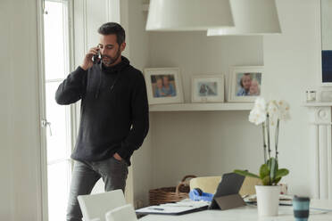 Mann arbeitet von zu Hause aus und spricht mit seinem Smartphone am Fenster - CAIF30275