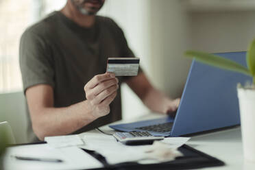 Mann mit Kreditkarte beim Online-Shopping am Laptop - CAIF30278