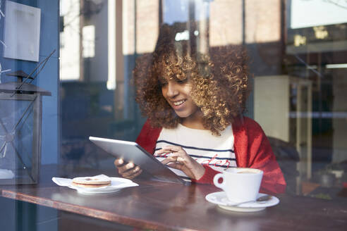 Smiling Afro woman using digital tablet while sitting at cafe - VEGF03671