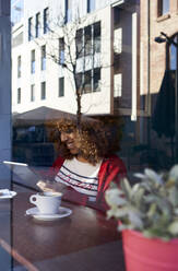 Young woman using digital tablet while sitting by window at cafe - VEGF03672