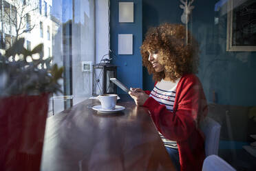 Frau lächelt, während sie in einem Café sitzt und ein digitales Tablet benutzt - VEGF03673