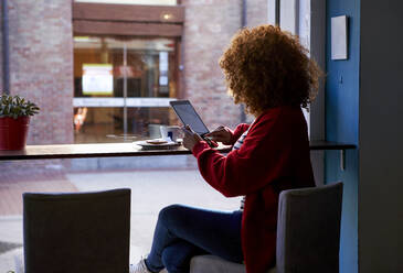 Junge Frau, die ein digitales Tablet benutzt, während sie in einem Café sitzt - VEGF03678